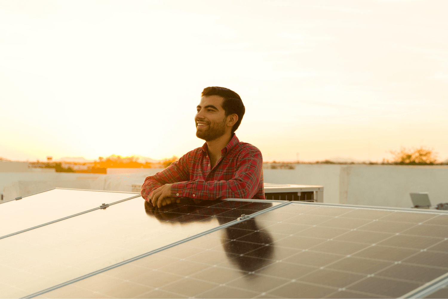 Ein Mann auf seinem Dach lehnt sich an seine Solaranlage im Sonnenaufgang